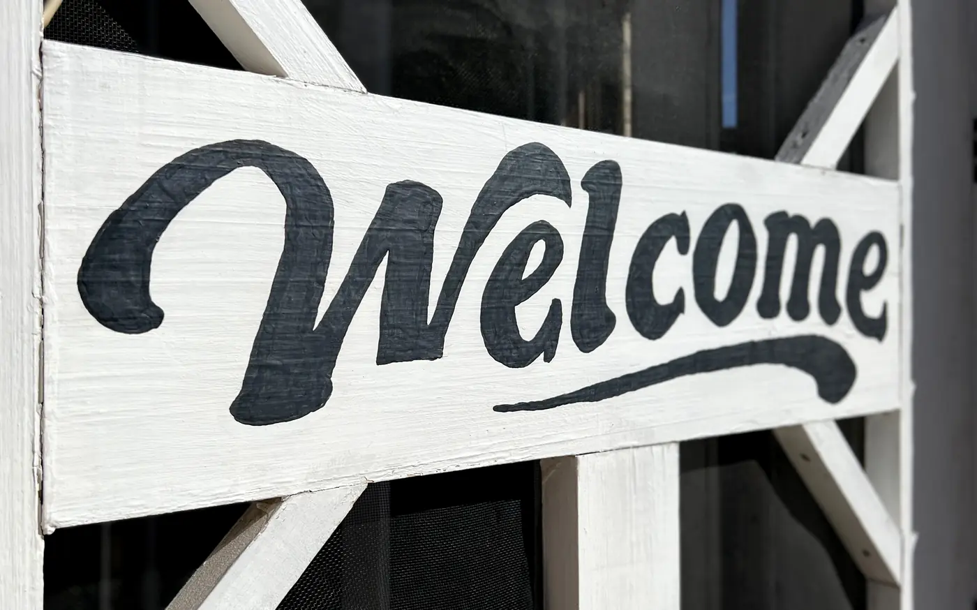 a wooden hinged screen door with a welcome sign hung on it